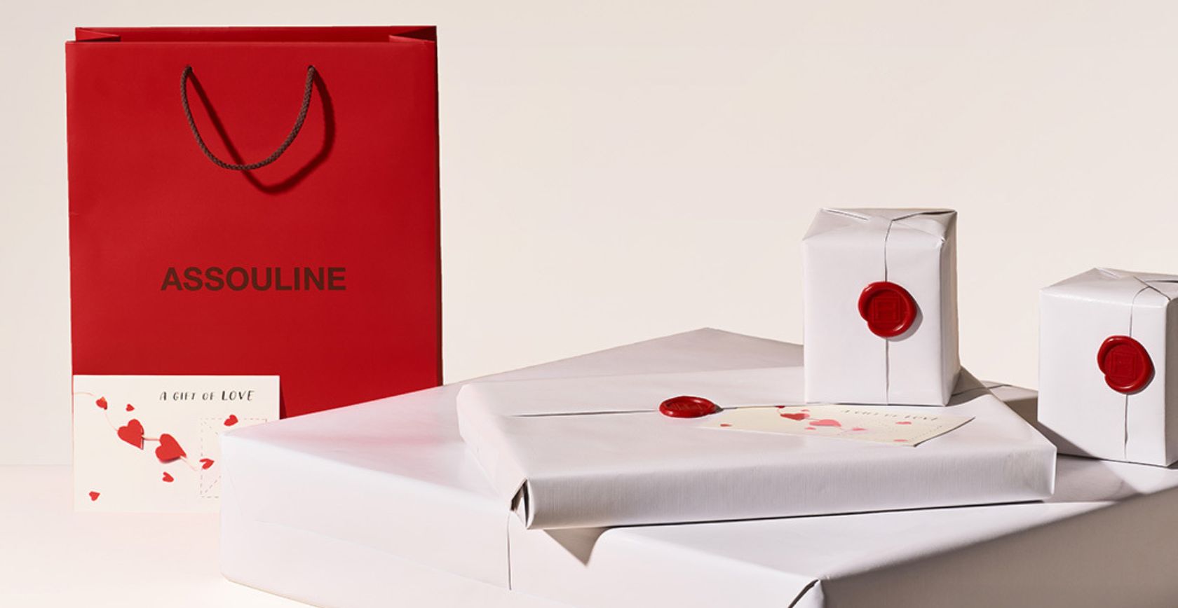 Assouline Gift Wrap 4 presents in white paper with a red wax seal, red gift bag and postcard