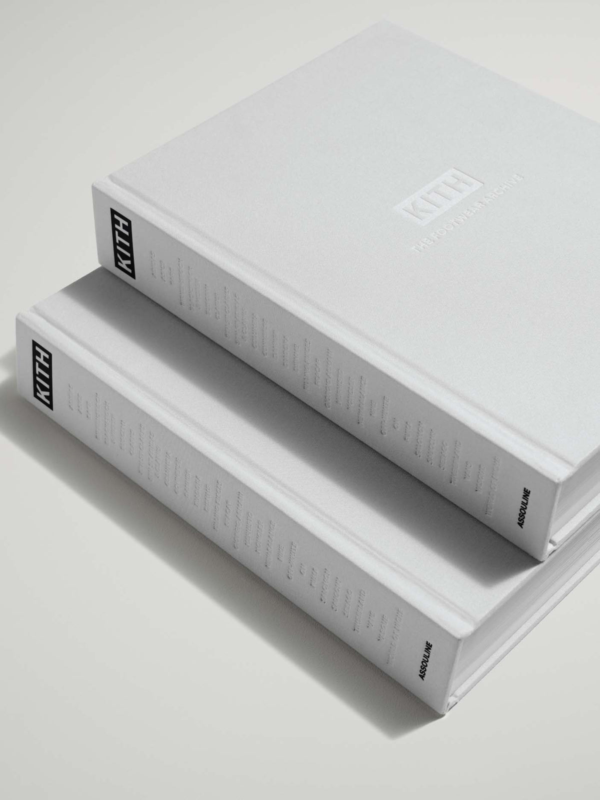 Two hardcover art books stacked diagonally on a light gray surface. The top book is white with 'KITH' printed on the spine and cover, and the bottom book shows its white spine with fine text.