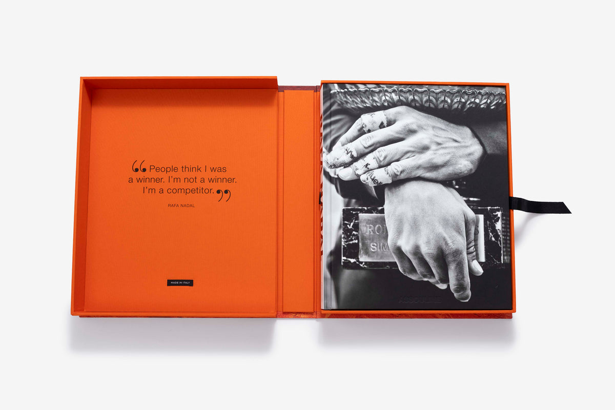 Rafa Nadal (Ultimate) by Assouline: straight-on view of the open orange presentation case, its lid printed with the quote, People think I was a winner, I'm not a winner, I'm a competitor, and the companion book resting in the base, black ribbon marker visible