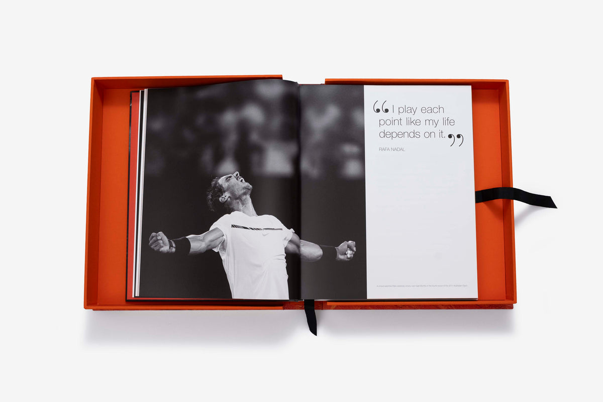 Rafa Nadal (Ultimate) by Assouline: the companion book open inside its orange presentation case, showing a black-and-white photograph of Rafa Nadal celebrating with arms raised on the left page and the pull quote, I play each point like my life depends on it, on the right page