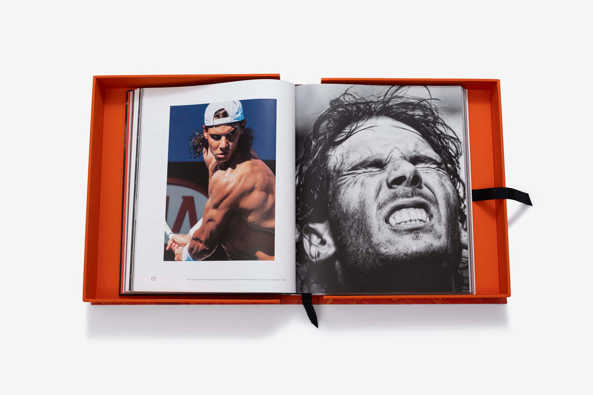 Rafa Nadal (Ultimate) by Assouline: the companion book open inside its orange presentation case, showing a color photograph of a shirtless Rafa Nadal in a white cap making a forehand swing on the left page and a black-and-white close-up portrait of him grimacing on the right page