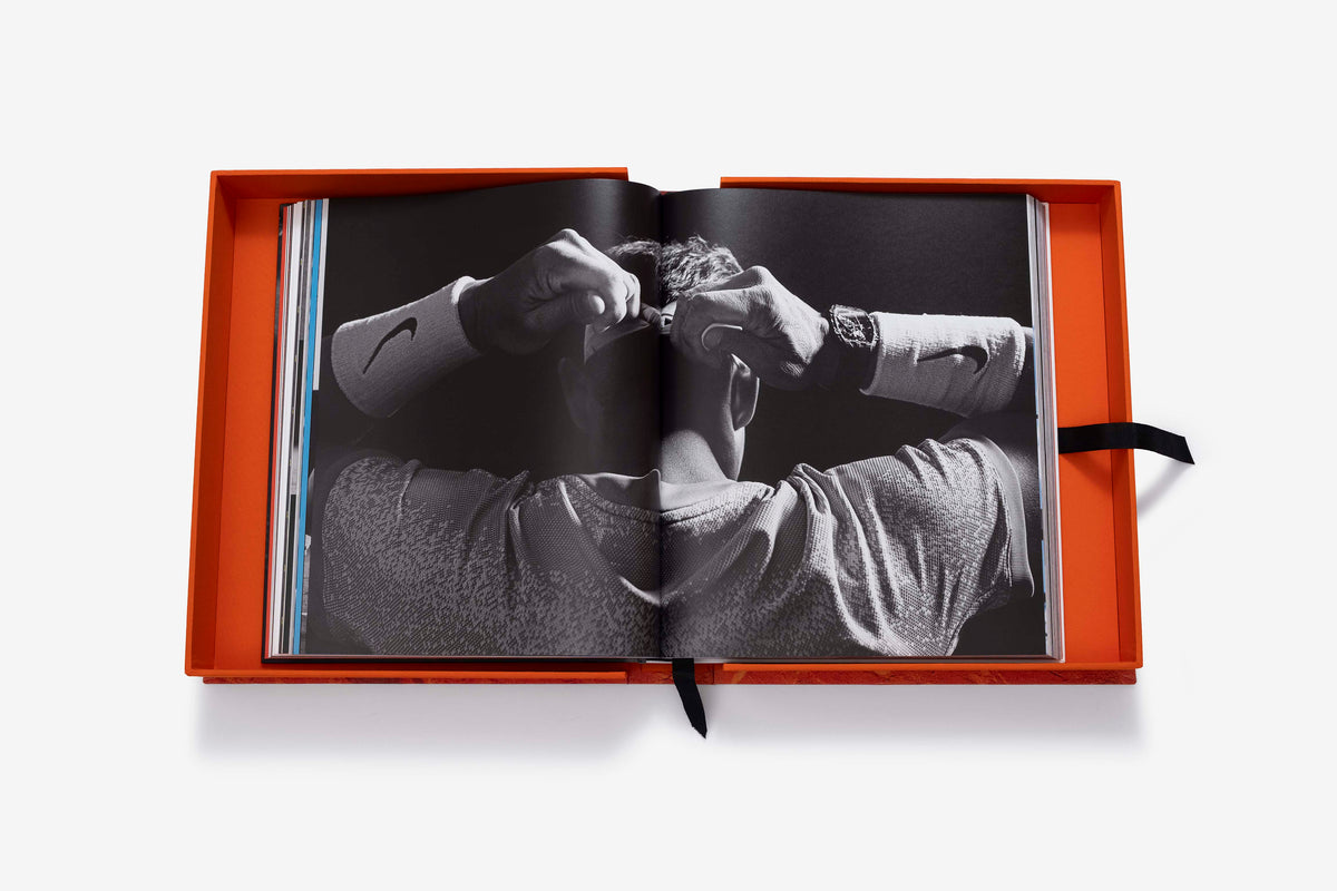 Rafa Nadal (Ultimate) by Assouline: the companion book open inside its orange presentation case to a black-and-white photograph, seen from behind, of Rafa Nadal adjusting his hair with both hands